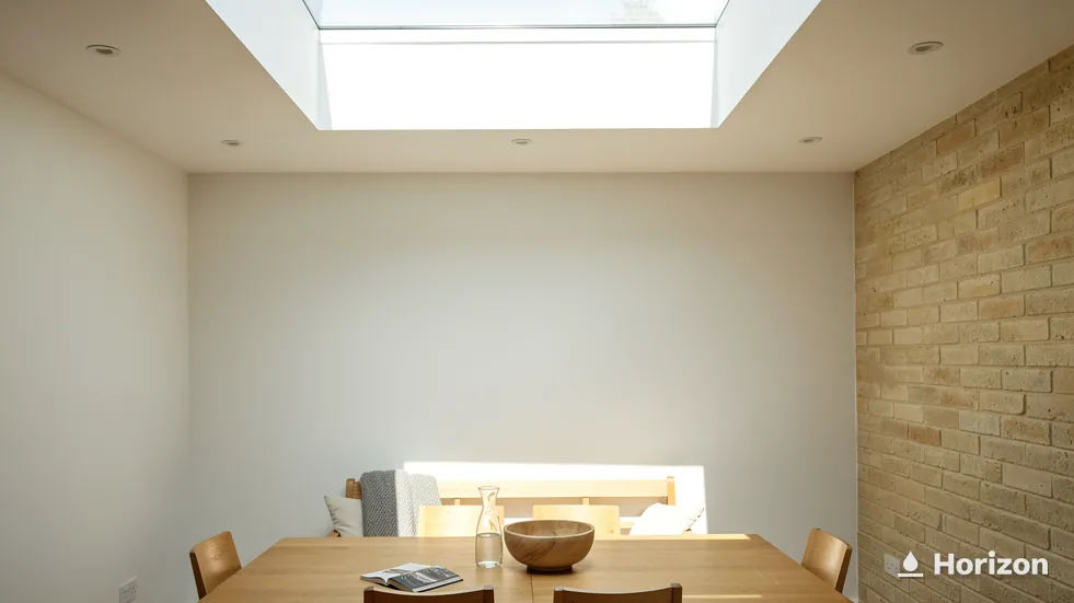 Simple dining room with a wooden table under a large flat rooflight and a stone side wall.