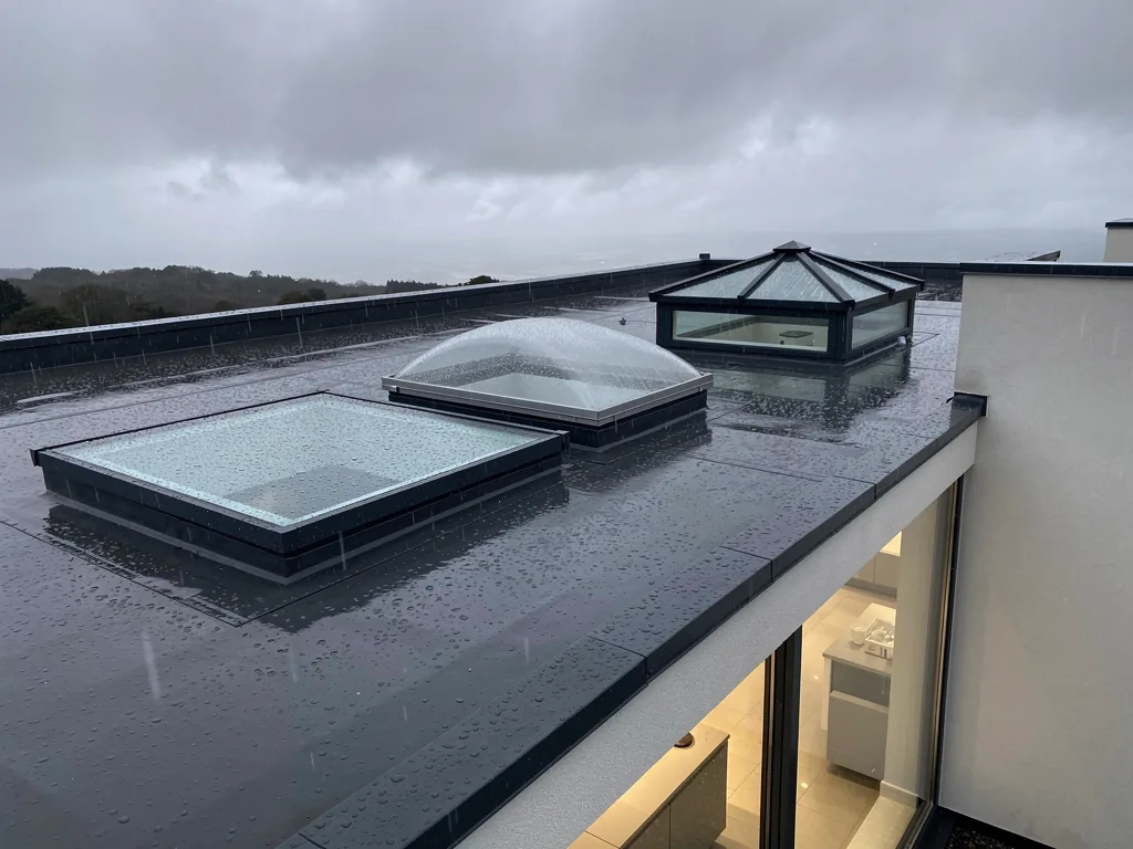 A flat glass rooflight, a domed rooflight and a small lantern side by side on a wet flat roof
