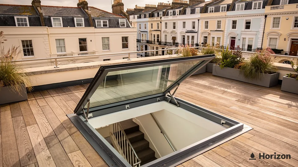 Hinged access rooflight open over a staircase on a timber roof terrace with planters.