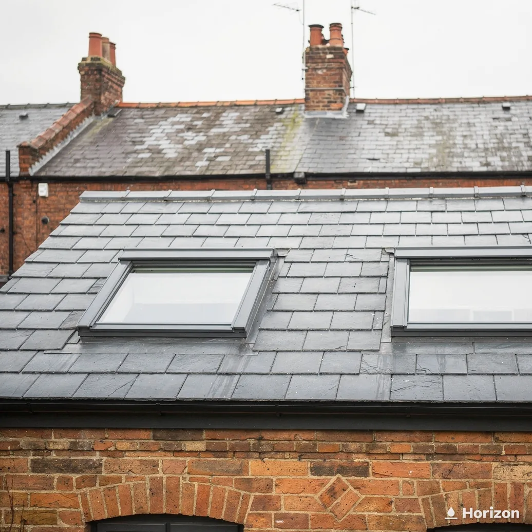 Two roof windows in the slate roof of a brick house with tall chimneys.