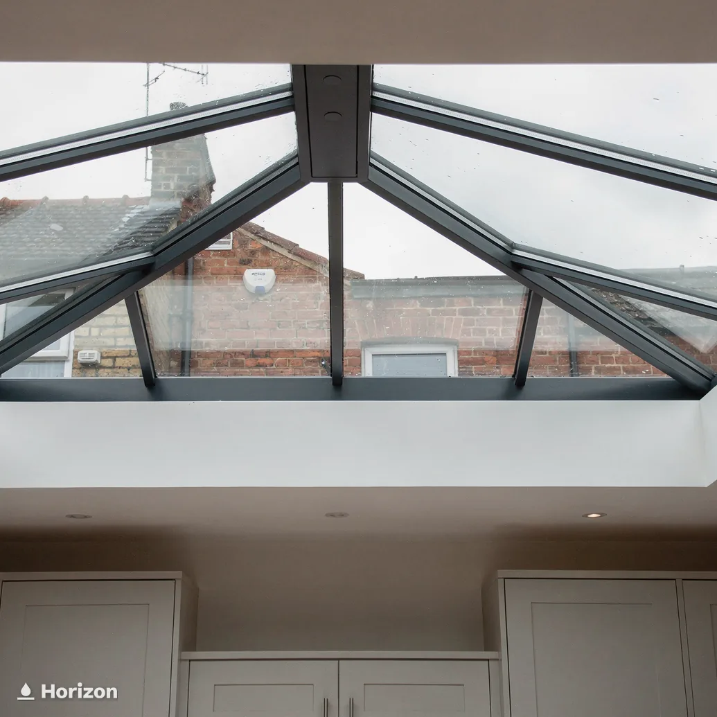 Looking up into a roof lantern with dark glazing bars and neighbouring roofs beyond.