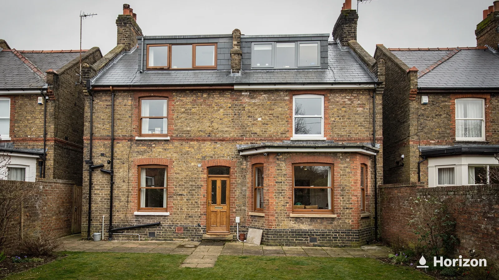 Rear of a brick house with a loft conversion, windows set into its slate roof and a lawn.