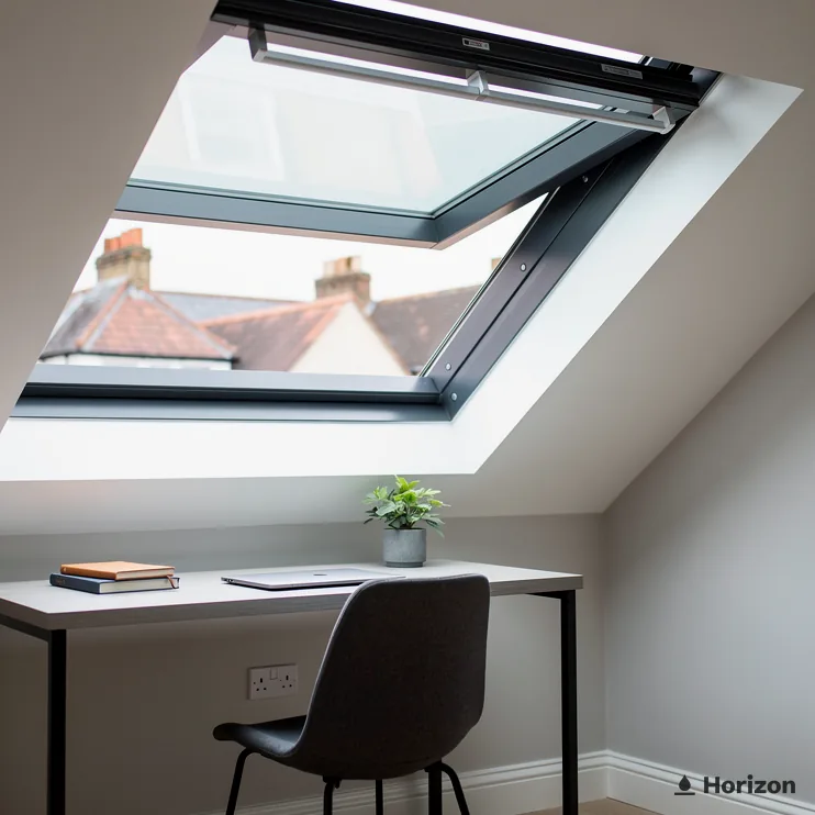 Home office desk and black chair beneath an open roof window showing rooftops.