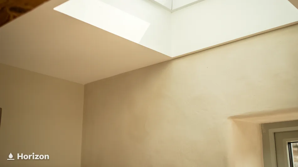 Plain plastered room lit by a deep rooflight opening in the ceiling.