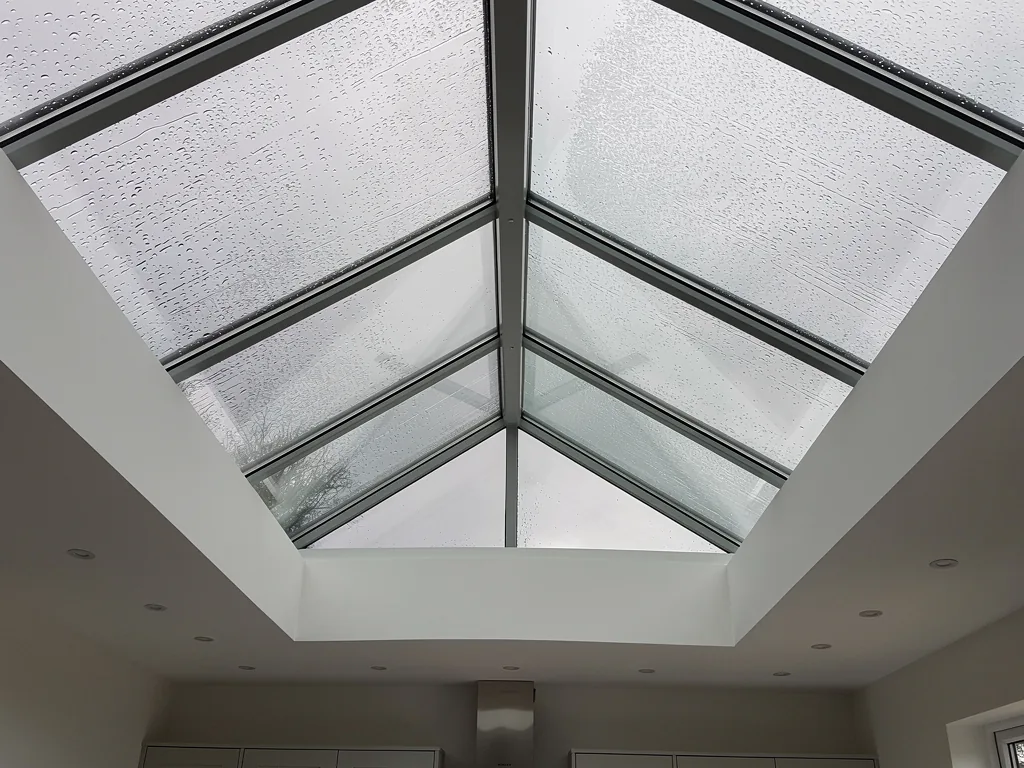 Looking up into a rectangular roof lantern with its central ridge and sloping glazing bars, rain on the glass