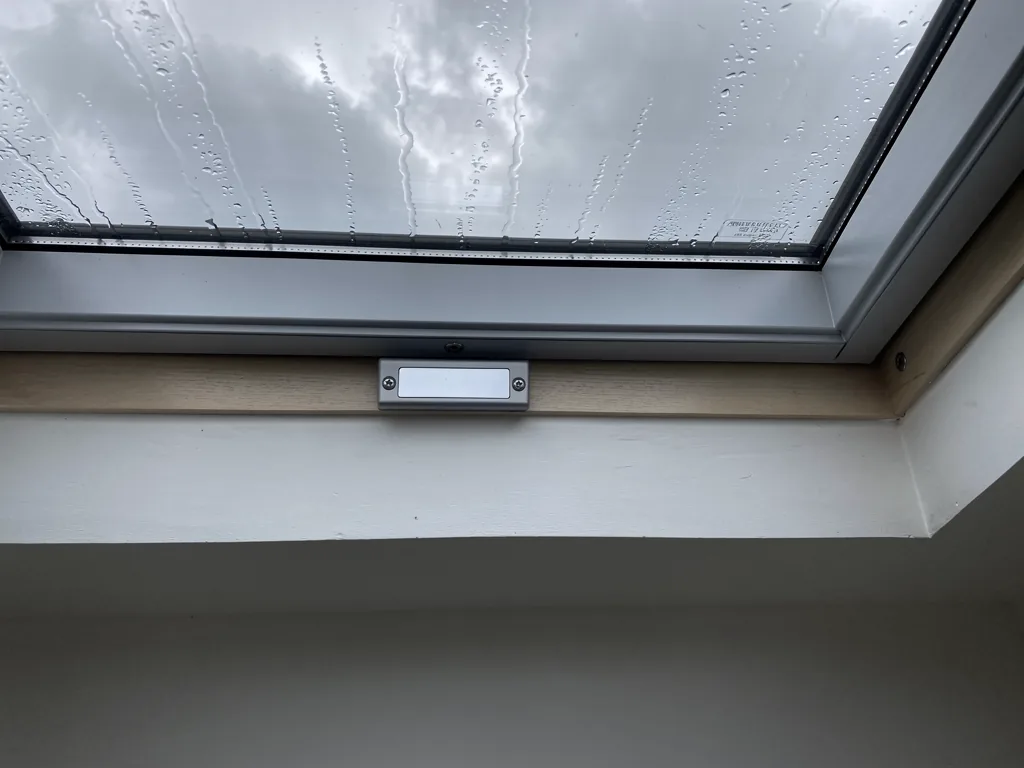 Close view of the inside frame of a roof window with a small blank data plate, rain on the glass