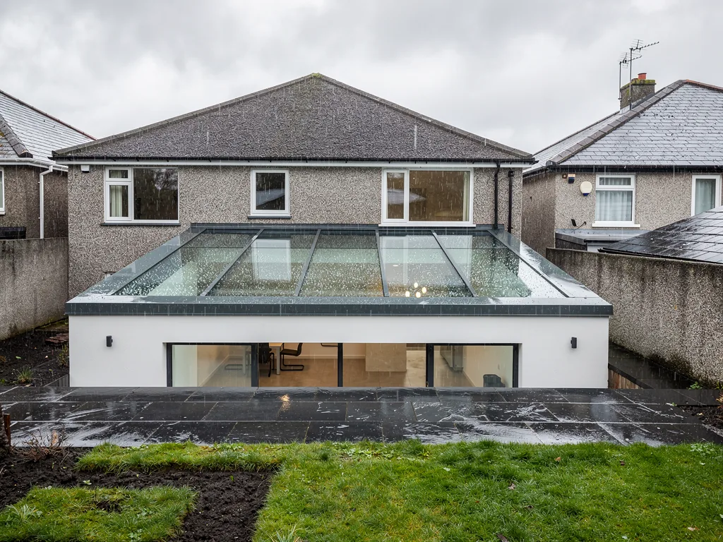 A pebble-dash semi with a flat-roof rear extension carrying a glass rooflight, wet garden